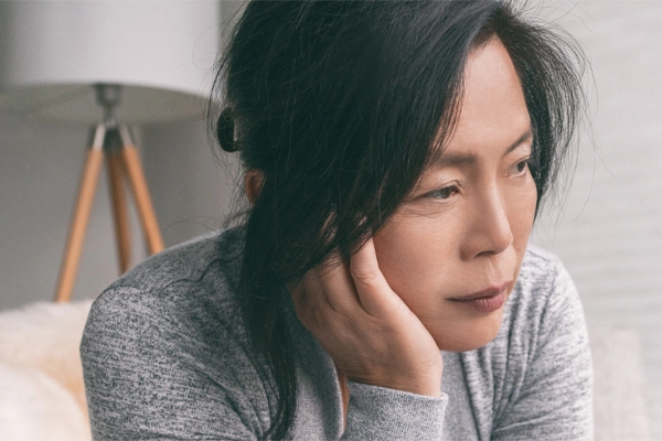 A middle-aged asian woman sitting on her couch, resting her head on her hand, suffering from adrenal fatigue. Get treatment for adrenal fatigue syndrome from Shelley Cole, M.D. of Healthy Success in Temple, Texas.