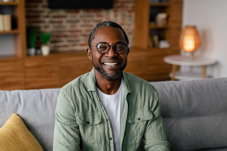 A middle aged black man in a green button up shirt sits on his couch smiling, happy with his treatment for andropause and low testosterone from Shelley Cole, M.D. of Healthy Success in Temple, Texas.