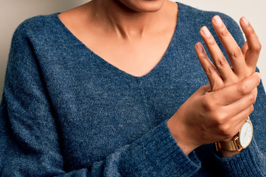 Close up of a woman in a blue sweater massaging one aching hand with the other. Get help for arthritis from Shelley Cole, M.D. of Healthy Success in Temple, Texas.