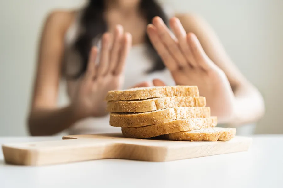 Close up of a stack of bread slices on a cutting board with a woman's hands behind them, refusing to eat. Get treatment for Celiac Disease from Shelley Cole, M.D. of Healthy Success in Temple, Texas.