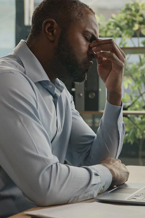 A black man rubbing the top of his nose at his desk, in need of chronic fatigue treatment from Shelley Cole, M.D. of Healthy Success in Temple, Texas.
