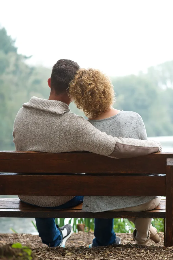 A man with his arm around a woman are shown from behind sitting on a bench on a serene morning. Get integrative medicine treatment from Shelley Cole, M.D. of Healthy Success in Temple, Texas.
