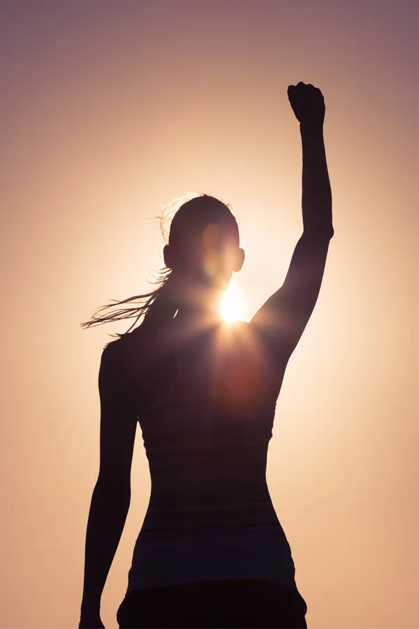 A woman raises her arm triumphantly, silhouetted by the sunset. Get Methylene Blue IV therapy from Shelley Cole, M.D. of Healthy Success in Temple, Texas.