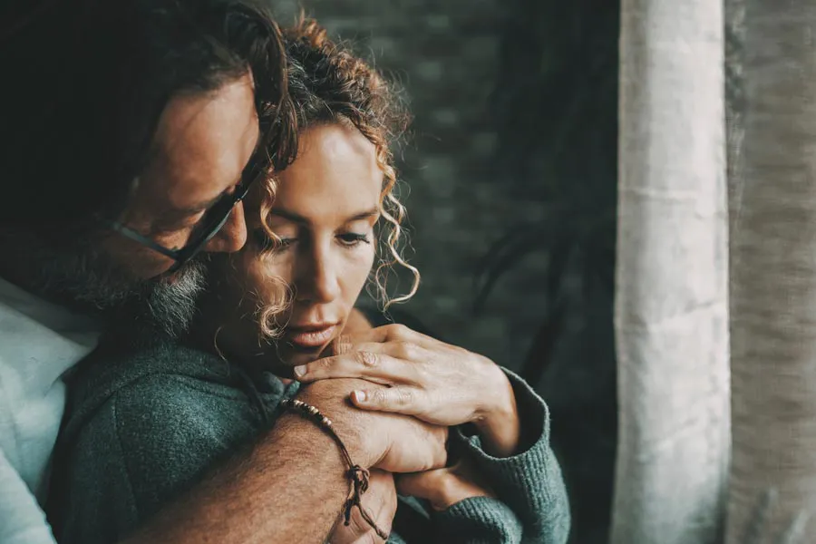 A man embraces a woman from behind in a dimly lit room, their somber expressions showing concerns about a neurodegenerative disease they will get treated by Shelley Cole, M.D. of Healthy Success in Temple, Texas.