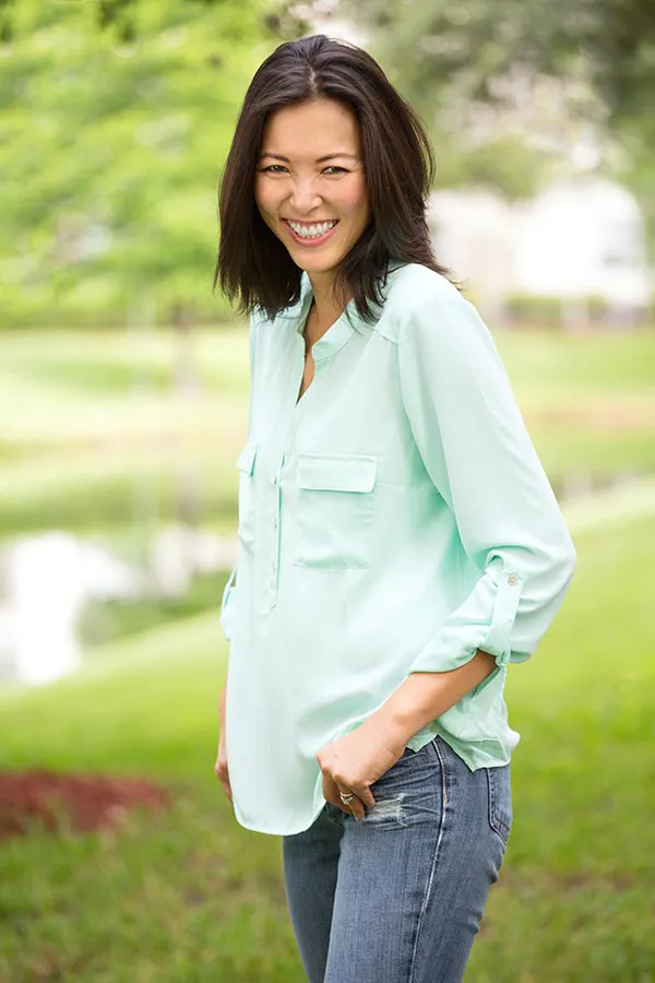 A middle-aged brunette woman in a light green button-up shirt stands outside smiling, happy with her perimenopause treatment from Shelley Cole, M.D. of Healthy Success in Temple, Texas.