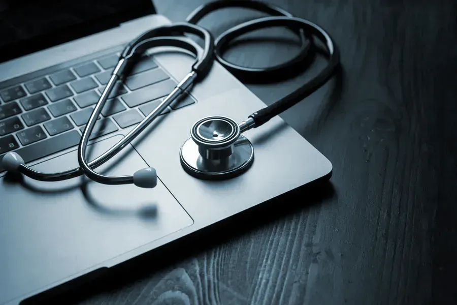 An open laptop with a stethoscope lying on it on a wooden table, symbolizing telemedicine care from Shelley Cole, M.D. of Healthy Success in Temple, Texas.