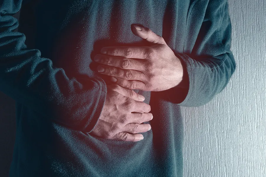 Close-up of the midsection of a man in a green sweater clutching his gut in pain. Get treatment for Ulcerative Colitis from Shelley Cole, M.D. of Healthy Success in Temple, Texas.