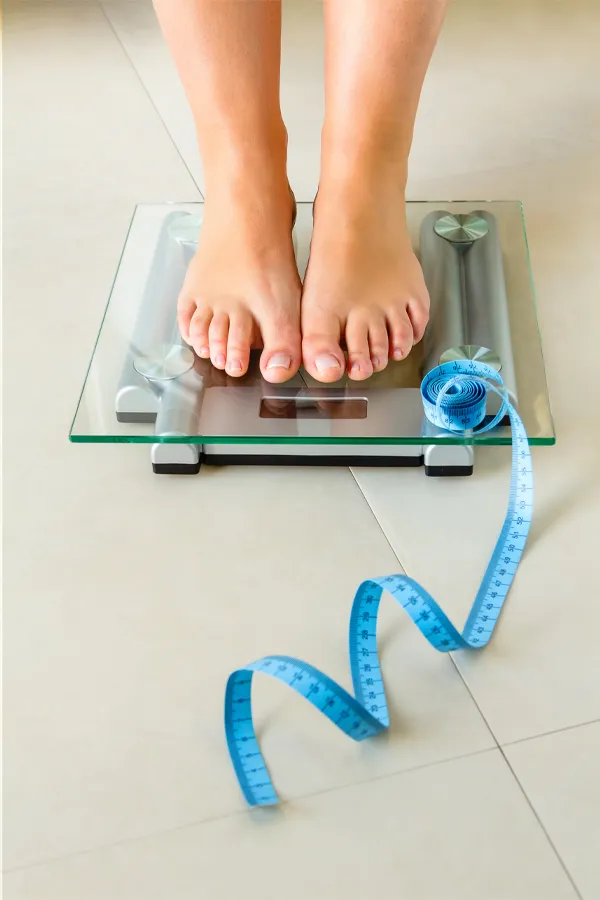 Close-up of a woman's feet standing on a scale, with measuring tape by her toes, getting treatment for weight loss resistance from Shelley Cole, M.D. of Healthy Success in Temple, Texas.